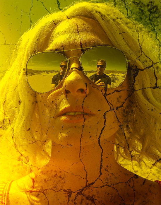 The reflection of a man smoking in a blonde woman's mirrored sunglasses