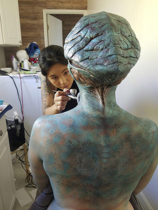 makeup artist applying body paint and alien prosthetics on actor
