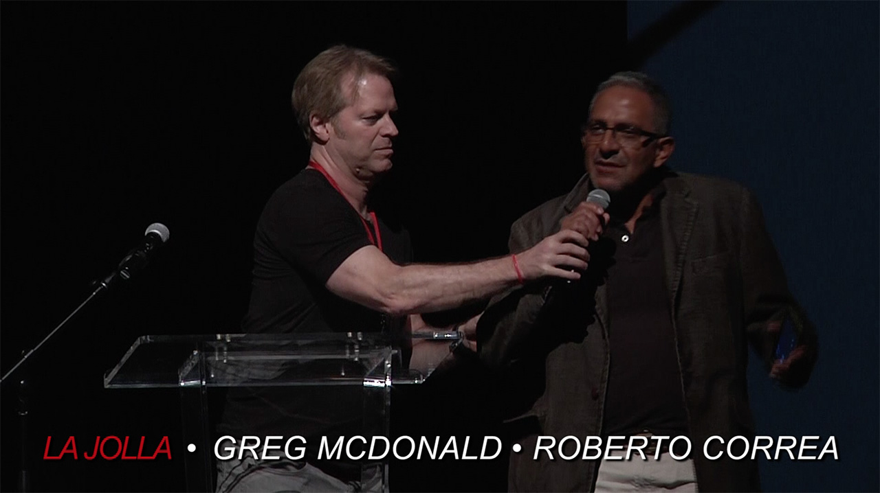 fashion film director Greg McDonald helps Roberto Correa hold the microphone correctly on stage at the La Jolla Fashion Film Festival.