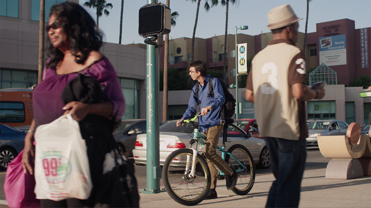 a man on a bike and two other people look frozen in time at a city street intersection while they wait for the light to change