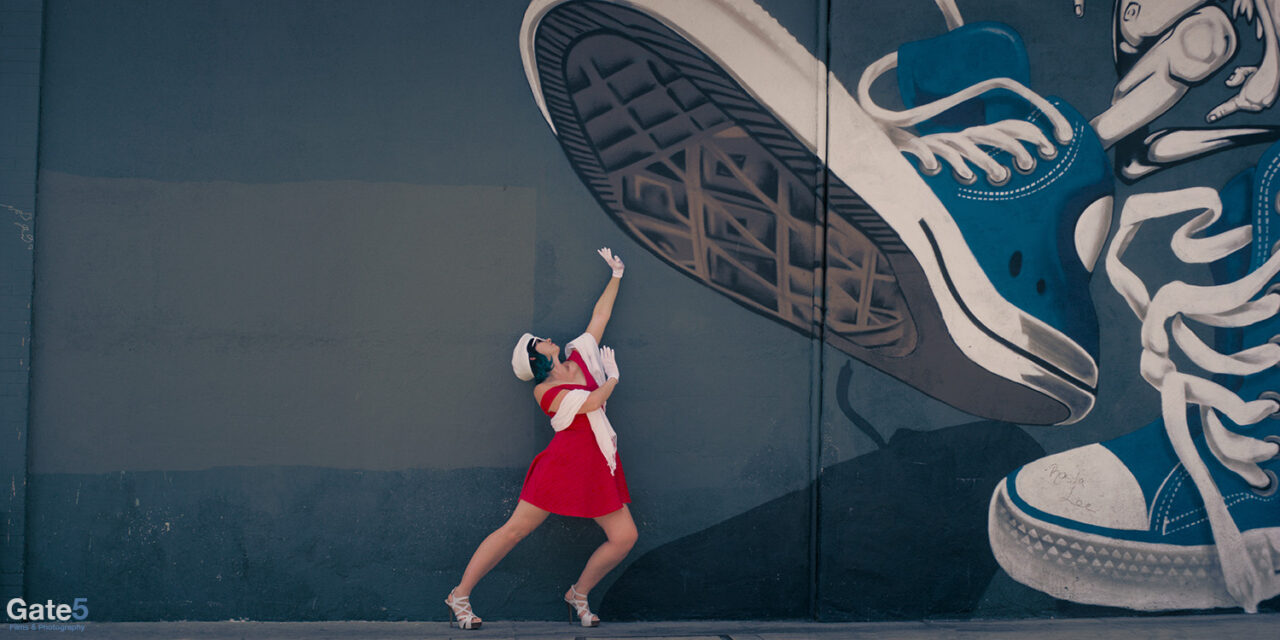 a French model interacts with a wall mural that looks like it's going to squash her underneath giant sneakers