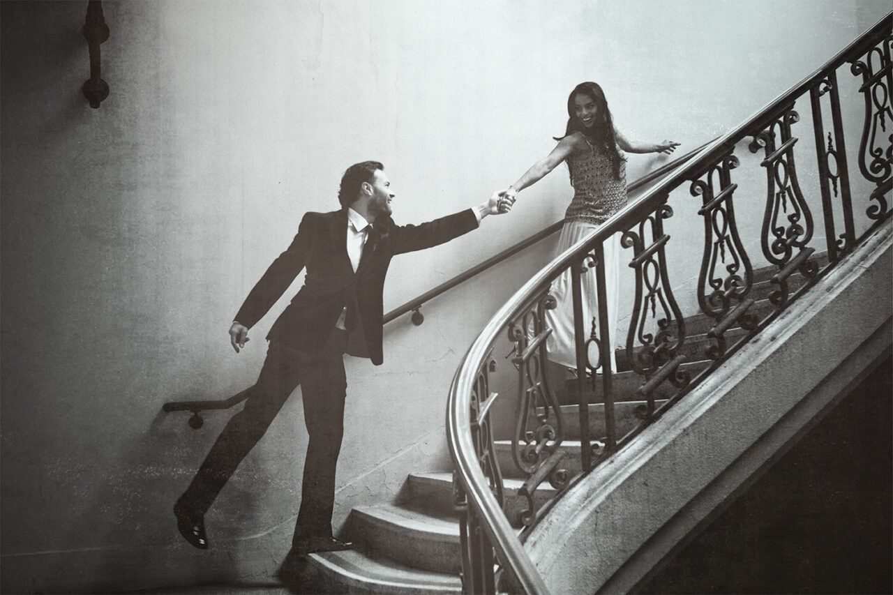faded black and white shot of two happy smiling lovers holding hands on an elegant staircase